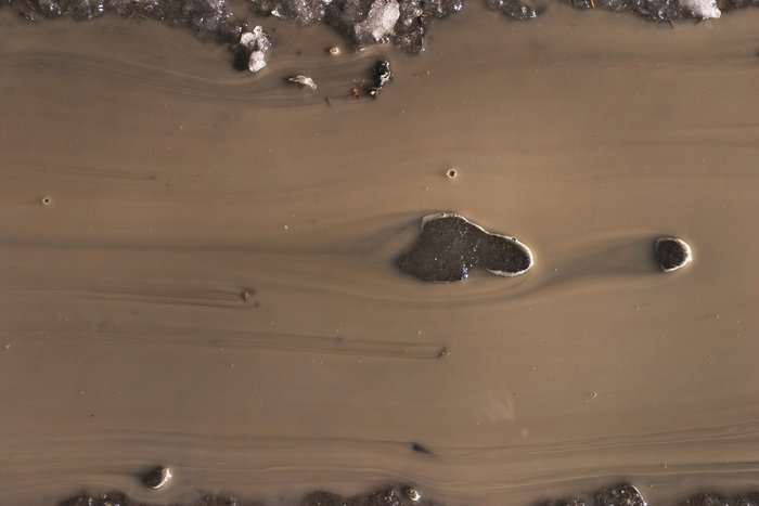 Muddy ice on the road melts and flows between puddles.  A thin, slow flow, in combination with the higher viscosity imparted by the mud, lead to nearly laminar flow.