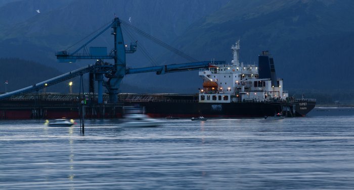 Boats race out of the Seward harbor for the 6AM opening of the Silver Salmon Derby, with the coal ship loading just behind them.
