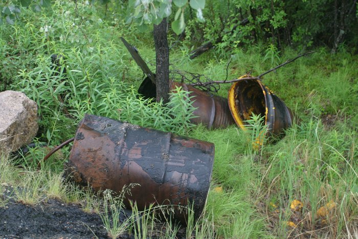These drums are dumped off the highway into Alaska.  Some are out in the open, others are partially or completely buried and rusting away.