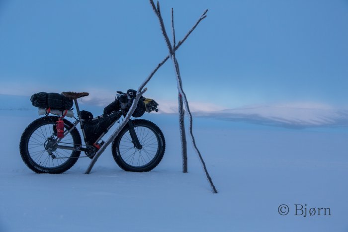 Carver fat-bike leaning on a trail marker as the ice fog lifts to reveal dawn light.